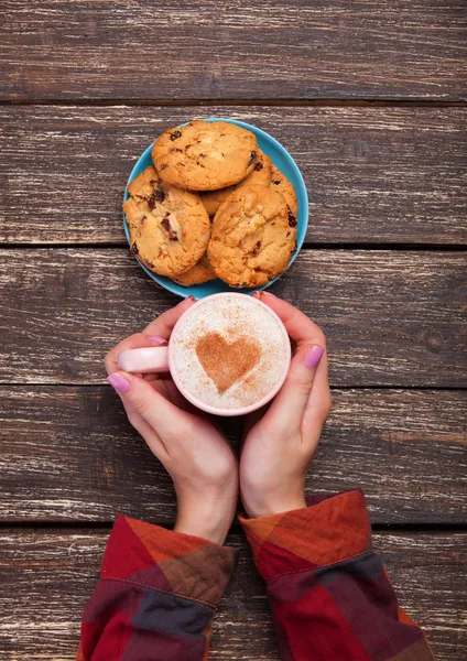 Female hands holding cup of coffee and cookies on wooden table. — Stock Photo, Image