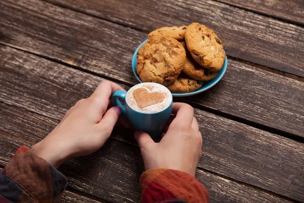 Manos femeninas sosteniendo taza de café y galletas en la mesa de madera . — Foto de Stock