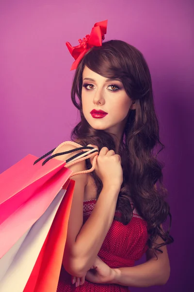 Beautiful brunette girl with shopping bags on violet background. — Stock Photo, Image