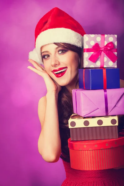 Красива брюнетка в різдвяній шапці з подарунками на фіолетовому б — стокове фото
