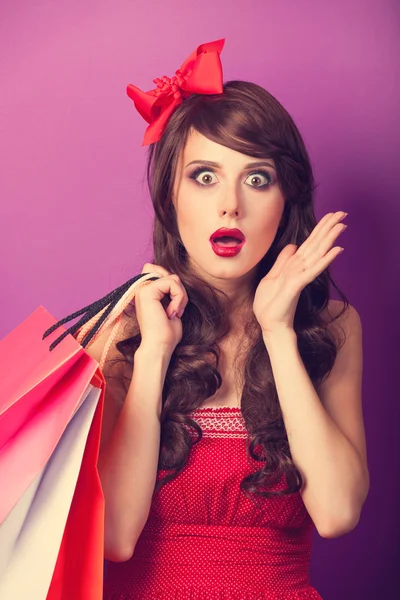 Beautiful brunette girl with shopping bags on violet background. — Stock Photo, Image