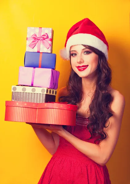 Beautiful brunette girl in christmas hat with gift on yellow bac — Stock Photo, Image