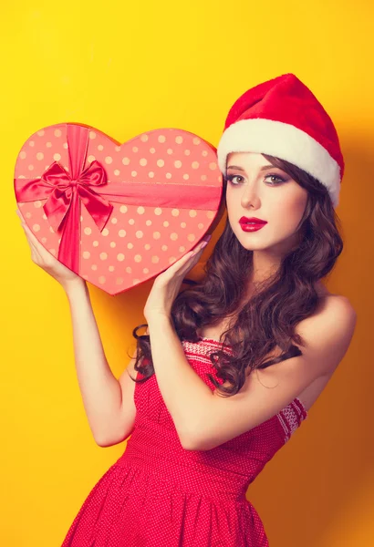 Mooie brunette meisje in kerstmuts met gift op gele bac — Stockfoto