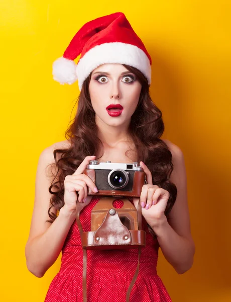 Mooie brunette meisje in kerstmuts met camera op gele b — Stockfoto