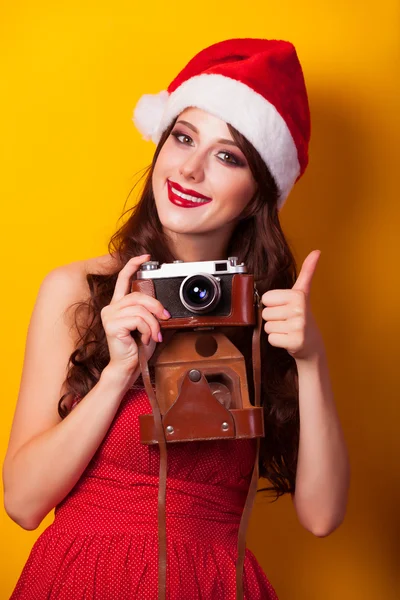 Mooie brunette meisje in kerstmuts met camera op gele b — Stockfoto