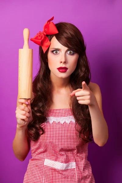 Beautiful brunette housewife with rolling pin on violet backgrou — Stock Photo, Image