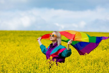 Baharda sarı kolza tohumu tarlasında LGBT gökkuşağı bayrağı taşıyan kadın