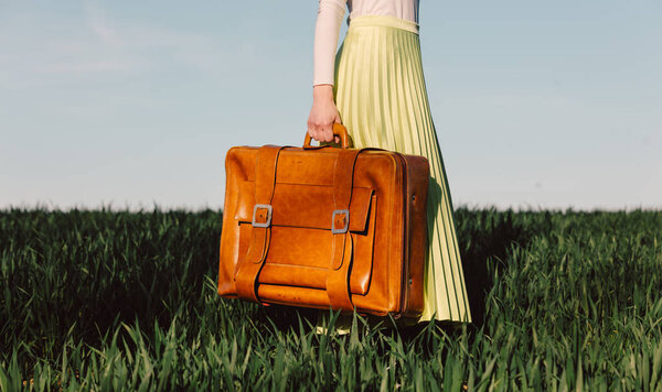 Женщина в зеленой юбке держит чемодан на пшеничном поле 