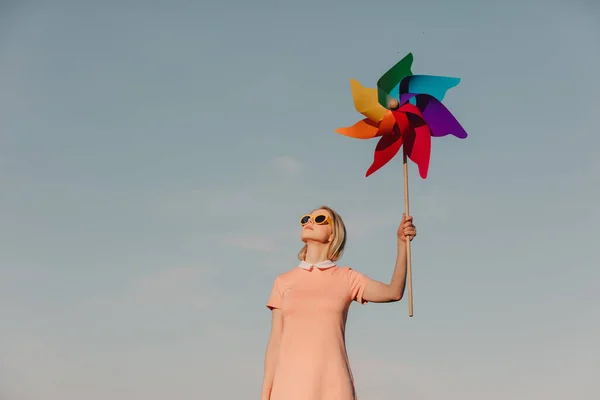 穿着粉色衣服 戴着黄色眼镜的时尚女人 手握蓝天背景的飞轮 — 图库照片