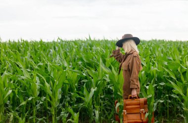 Yazın mısır tarlasında pelerinli ve şapkalı sarışın bir kadın.