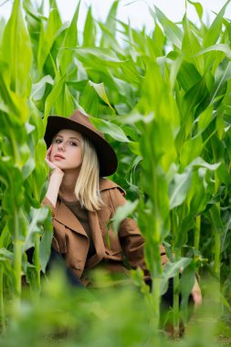 Yazın mısır tarlasında pelerinli ve şapkalı sarışın bir kadın.