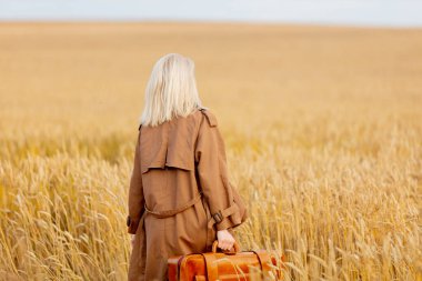 Buğday tarlasında bavullu sarışın kadın.