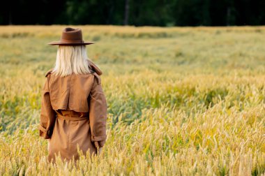 Buğday tarlasında pelerinli ve şapkalı sarışın kadın. 