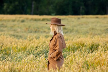 Buğday tarlasında pelerinli ve şapkalı sarışın kadın. 