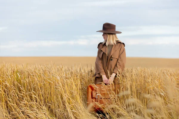ブロンド女性でクロークと帽子でスーツケースで小麦畑 — ストック写真