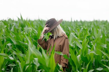 Yazın mısır tarlasında pelerinli ve şapkalı sarışın bir kadın.