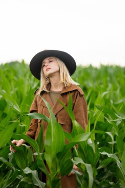 Yazın mısır tarlasında pelerinli ve şapkalı sarışın bir kadın.