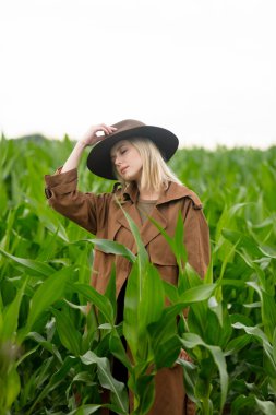Yazın mısır tarlasında pelerinli ve şapkalı sarışın bir kadın.