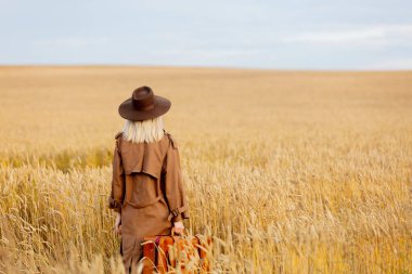 Buğday tarlasında pelerinli ve şapkalı sarışın kadın. 