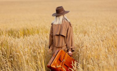 Buğday tarlasında pelerinli ve şapkalı sarışın kadın. 
