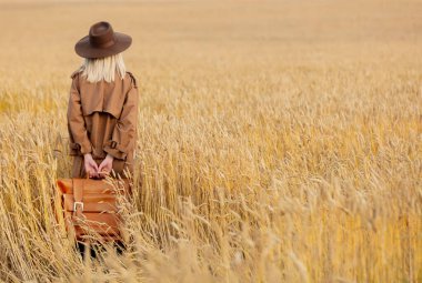 Buğday tarlasında pelerinli ve şapkalı sarışın kadın. 