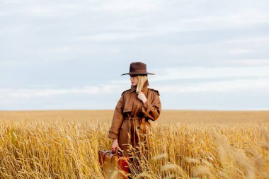 Buğday tarlasında pelerinli ve şapkalı sarışın kadın. 