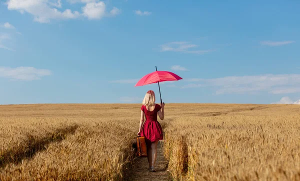 穿着红色衣服的金发姑娘 带着雨伞和手提箱在麦田里 — 图库照片