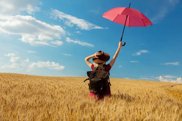 ブロンド女の子で帽子と赤いドレスで傘とバックパックで小麦畑 — ストック写真