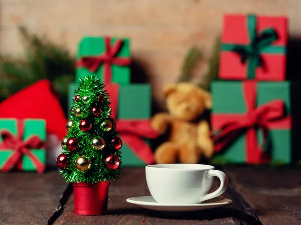 在木制桌子上的礼物旁边 有一杯咖啡和圣诞树 — 图库照片