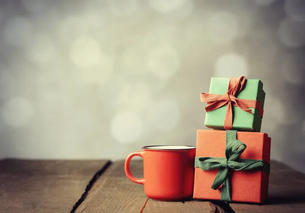 Red cup of coffee and gift boxes on wooden table with bokeh