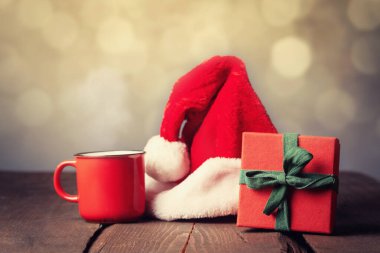 Kırmızı hediye kutusu ve Noel Baba şapkası arka planda Bokeh olan ahşap masada.