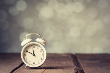 Ahşap masada beyaz alarmlı saat ve arka planda bokeh