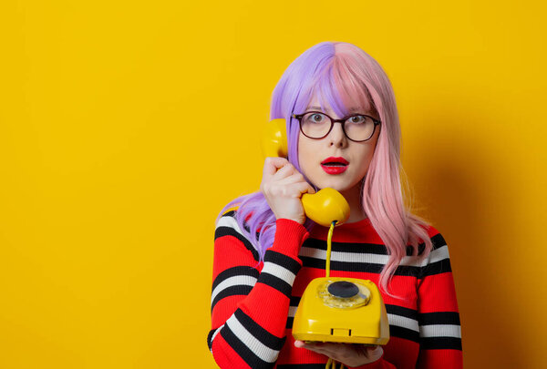 Girl with purple hair and red sweater hold dial phone on yellow background