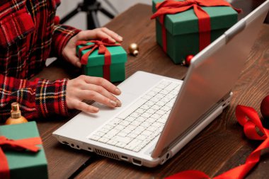 Dizüstü bilgisayarla çalışan ve hediye kutularını masaya saran bir kadın..
