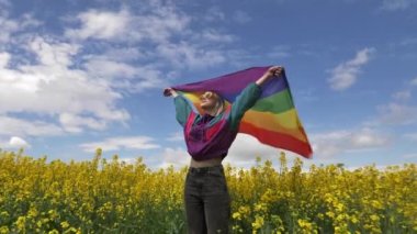 Baharda sarı kolza tohumu tarlasında LGBT gökkuşağı bayrağı taşıyan kadın