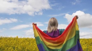Baharda sarı kolza tohumu tarlasında LGBT gökkuşağı bayrağı taşıyan kadın
