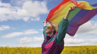 Baharda sarı kolza tohumu tarlasında LGBT gökkuşağı bayrağı taşıyan kadın