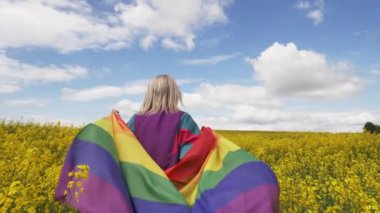 Baharda sarı kolza tohumu tarlasında LGBT gökkuşağı bayrağı taşıyan kadın
