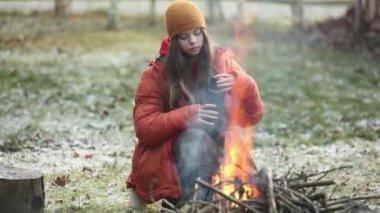 Kampta şenlik ateşinin yanında oturan kupalı genç kız.