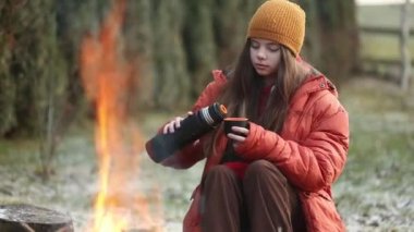 Kampta şenlik ateşinin yanında oturan kupalı genç kız.