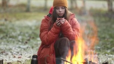 Kampta şenlik ateşinin yanında oturan kupalı genç kız.