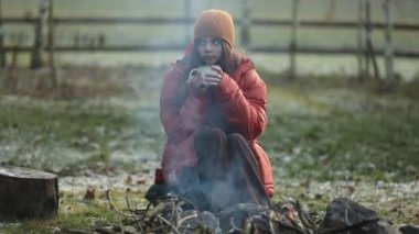 Kampta şenlik ateşinin yanında oturan kupalı genç kız.