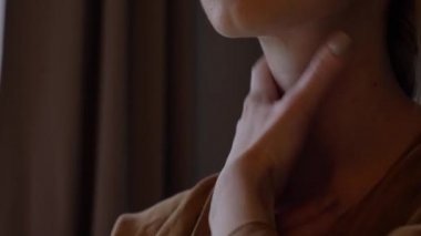 Orta yaşlı kadın aynanın yanındaki masada oturuyor ve yüz masajı yapıyor.