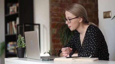 Dizüstü bilgisayarı olan gözlüklü bir kadın evde oturuyor ve çalışıyor.