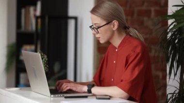 Gözlüklü beyaz kadın evden bilgisayarla çalışıyor, uzaktan kumandalı.