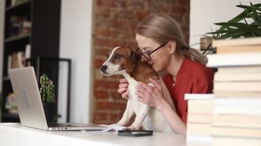 Evde dizüstü bilgisayarda çalışan köpeği olan genç bir kadın.