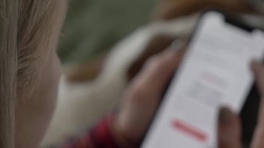 Cep telefonuyla internette sörf yapan, Jack Russell Terrier köpeğiyle kanepede yatan bir kadın.
