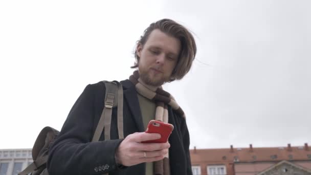 stylish man in a scarf and black coat uses a cell phone on a city street of Wroclaw, Poland