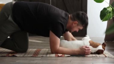 Adam evde bir köpeğin yanında sağlık için egzersiz yapmaya çalışıyor.