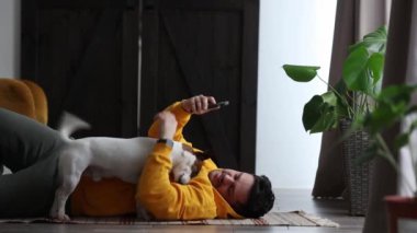 Evde köpek ve akıllı telefonla yerde yatan bir adam.